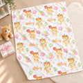 A personalized baby blanket with a white background, printed with cartoon orange tabby cats, pink stars, green balloons, and the name 'Riley' in gold script. The blanket is styled on a light wood floor next to a plush toy, a gift box, and a soft cream rug.