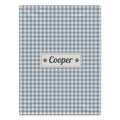 A rectangular personalized dog blanket with a light blue and white gingham check pattern, featuring a central cream label with the name 'Cooper' in navy blue script and navy paw prints on either side, shown on a plain white background.