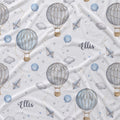 A white fabric with a repeating pattern of watercolor hot air balloons, clouds, stars, blue balloons, and the name 'Ellis' in gray script.