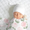 Newborn wearing a white knotted hat, wrapped in a Blush Rose Garden swaddle with pink roses, sage leaves, and Elizabeth Rose lettering.