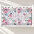 A white changing table with a personalized changing pad cover featuring a floral-patterned mattress protector with pink roses, green leaves, and the name 'Skylar' in pink script.