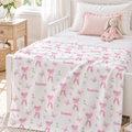 A white baby blanket with pink ballet dancer bows, butterflies, and the name 'Isabelle' printed in pink, styled on a white single bed in a bright nursery with a pink bunny plush toy.