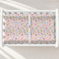 A white changing table with a personalized changing pad cover featuring a pastel floral and butterfly pattern. The fabric are personalized with the names 'AMELIA' and 'grace' in blue script.