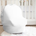 A white baby car seat cover fitted over a car seat, placed in a nursery setting in front of a white crib on a white faux fur rug.