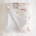 A personalized baby blanket with a white sherpa backing and a cream printed front featuring a gnomes, candy canes, and the name 'CHARLOTTE anna' in red and black script, laid flat on a white faux fur background.