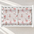 A white changing table with a personalized changing pad cover featuring a repeating pattern of cute cartoon bunnies in pink and red, with the text 'CHARLOTTE Anne' printed on the fabric.
