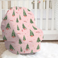 A pink baby car seat cover with a Christmas tree pattern, placed on a white faux fur rug in front of a white crib.