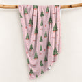 Personalized Christmas swaddle blanket hanging on a wooden rail with watercolor Christmas trees, presents and custom baby name.