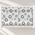 A white changing table with a personalized changing pad cover featuring white background and a green Christmas wreath pattern with red bows.