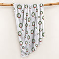 Personalized Christmas swaddle blanket hanging on a wooden rail with watercolor holiday wreaths, red bows and custom name Jack Wyatt.