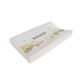 A contoured baby changing pad cover in a light gray fabric with a printed design of yellow construction vehicles and the name 'MASON' in dark gray, shown on a plain white background.