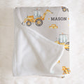 A personalized baby blanket with a white sherpa reverse and a printed front featuring yellow construction vehicles, bricks, and the name 'MASON' on a soft white faux fur background.
