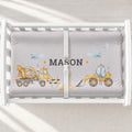 A white changing table with a personalized changing pad cover featuring a light gray background with yellow construction vehicles and the name 'MASON' in the center.