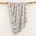 Personalized swaddle blanket hanging on a wooden rail with watercolor construction trucks, excavators, cement mixers and custom name Mason.