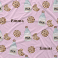 A close-up of a pink fabric with a repeating pattern of chocolate chip cookies, milk bottles, and the name 'Emma' in brown text.