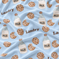 Light blue fabric with a repeating pattern of cartoon milk bottles, chocolate chip cookies, and the word 'Landry' in brown script.