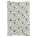 Pale sage swaddle blanket with white narcissus flowers, scattered green leaves, and the name Clara Noelle repeated in rose and green.