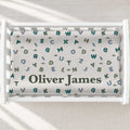 Customized baby changing pad cover featuring an alphabet and cactus pattern in teal, green, and blue on a white background, with the name 'Oliver James' printed in dark green. The bedding is displayed inside a white changing table.