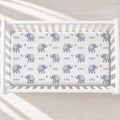 A white crib mattress fitted sheet with a repeating pattern of gray baby elephants and the word 'river' in small black text, shown inside a white wooden crib.