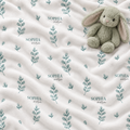 A close-up of a soft cream-colored fabric with a repeating pattern of muted blue-green leaf sprigs and the name 'SOPHIA maria' printed in small gray text. A plush gray bunny toy rests on the upper right side of the fabric.