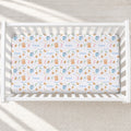 A fitted crib mattress with a whimsical pattern of teddy bears, stars, stars, and the name 'Emma' in blue, shown inside a white wooden crib.