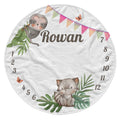 A personalized round white baby blanket featuring cute cartoon illustrations of a sloth and a baby fox, green leaves, colorful bunting, butterflies, and numbers 1 through 12 arranged around the edge. The name 'Rowan' is printed in the center.