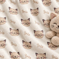 A plush cream-colored blanket with a repeating pattern of smiling cat faces and the name 'Iris' in cursive, styled with a matching plush cat toy on the right side.