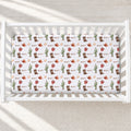 A white crib mattress fitted with a white sheet featuring a repeating western print of cacti, boots, hats, horseshoes, and the name 'WYATT' in a retro font, shown in a softly lit nursery setting.