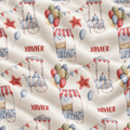 Personalized cream-colored fabric featuring a repeating watercolor pattern of popcorn carts, balloons, stars, bunting, and the name 'XAVIER' printed in red.