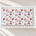 A white crib mattress fitted sheet with a colorful insect and butterfly pattern, personalized with the name 'Daisy Mae' in blue script, shown inside a white wooden crib.