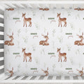 A personalized crib sheet with a repeating woodland print featuring brown deer illustrations, small wildflower motifs, and the words 'Dakota James' in brown script.