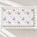 A white crib mattress fitted with a printed sheet featuring brown deer illustrations, small green leaves, and the names 'Dakota James' repeated across the surface, shown in a white crib on a light textured floor.