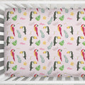 A crib sheet covered in a tropical pattern featuring toucans, green leaves, small yellow flowers, and the name 'Mae' in pink script, shown inside a white wooden crib.