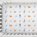 A white fitted crib sheet with a repeating space-themed print featuring astronauts, rockets, planets, stars, and the name 'FINN' in blue, shown inside a white wooden crib.