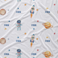 A white fabric with a repeating space-themed print featuring astronauts, rockets, planets, stars, and the name 'FINN' in blue text.