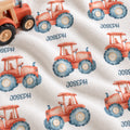 A close-up of a white fleece blanket printed with a repeating pattern of red-orange watercolor tractors with blue tires and the name 'JOSEPH' printed below each tractor.