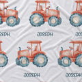 White fabric with a repeating pattern of orange-red watercolor tractors with blue-gray wheels and the name JOSEPH printed below each tractor.