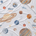 A white fabric blanket or sheet featuring a watercolor-style space print with planets, stars, and the personalized name 'Oliver James' printed in blue and orange text.
