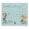 A personalized baby blanket featuring a light blue background with watercolor illustrations of two mermaids, a turtle, starfish, and a calendar grid with the names 'ANNA' and 'catherine' at the top.