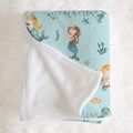 A personalized baby blanket with a white plush reverse side and a light blue printed front featuring mermaids, sea creatures, and the name 'Catherine'.