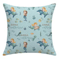 A square throw pillow with a light blue mermaid and underwater theme print, featuring the personalized name 'ANNA catherine' in brown and teal script. The pattern includes mermaids, dolphins, fish, and sea plants on a solid light blue background.