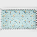 A crib mattress fitted sheet with a whimsical mermaid and dolphin pattern on a light blue background, personalized with the names 'ANNA' and 'catherine' in script.