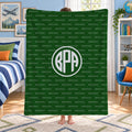 A person standing in a bedroom holding up a dark green blanket or throw featuring a repeating 'BROOKS' wordmark pattern and a large circular 'BPA' monogram in the center.