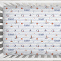 A crib mattress fitted sheet with a nautical theme, featuring the word 'SUNNY' in blue, sailboats, life preservers, seahorses, and orange starfish on a white background with light blue horizontal stripes.