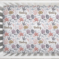 A crib mattress cover with a personalized nautical pattern featuring the name 'Finley' in brown script, decorated with seashells, starfish, anchors, and coral on a white background.