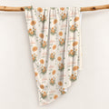 Cream swaddle blanket with golden-orange marigold clusters, green leaves, and the name Autumn Grace in orange and green.