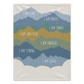 A personalized blanket featuring a layered mountain design in shades of blue, green, and mustard yellow, with white hand-lettered text reading positive affirmations like 'I AM KIND', 'I AM BRAVE', and 'I AM LOVED'.