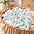 A mint green and white striped baby blanket with the name 'olivia' printed in script and small heart motifs, styled inside a large woven wicker basket.