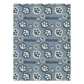 A personalized dog blanket featuring a repeating pattern of cream-colored paw prints and the word 'Winston' in dark gray on a dusty blue background.