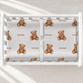 Personalized teddy bear changing pad cover with watercolor bears wearing bows and the name Rowan in brown, shown on a white changing table.